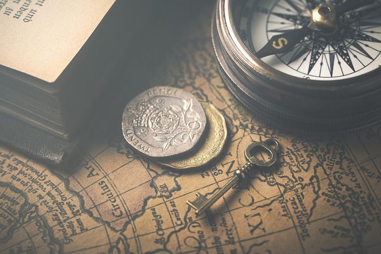 A printed map covers a desk on which likes a small key, a British 20 pence coin, stacked on a Mexican coin, with an analogue compass in the corner.